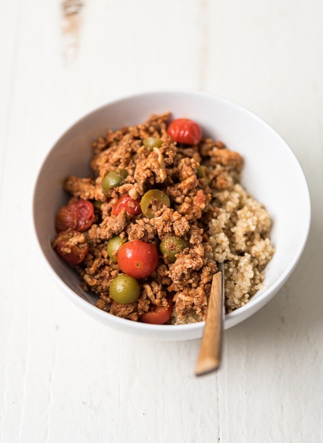 Cooked ground meat in a bowl with tomatoes, olives and served over quinoa