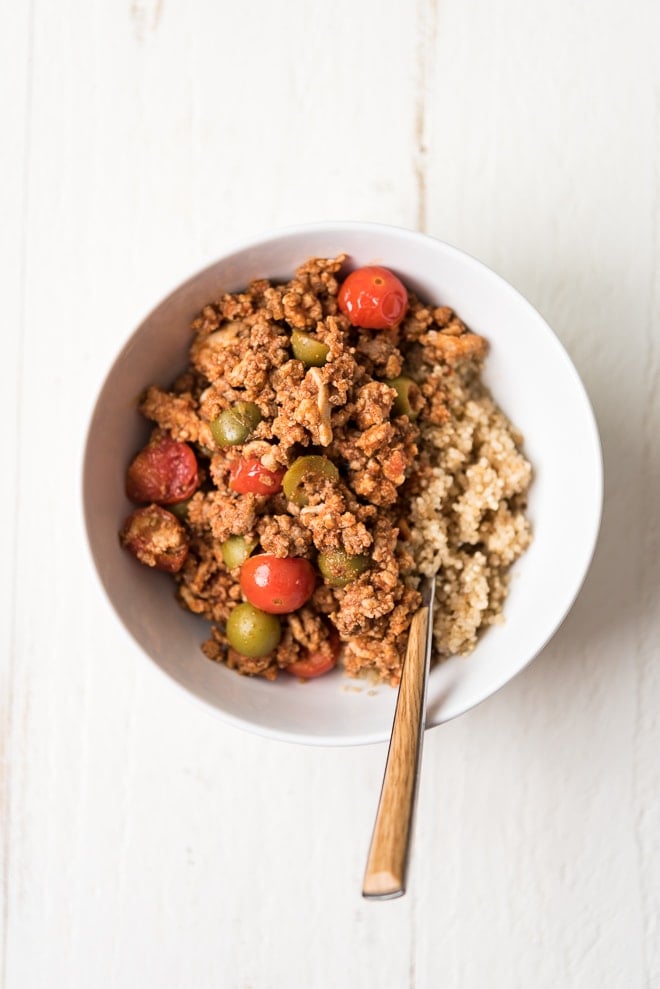 Cooked ground meat in a bowl with tomatoes, olives and served over quinoa