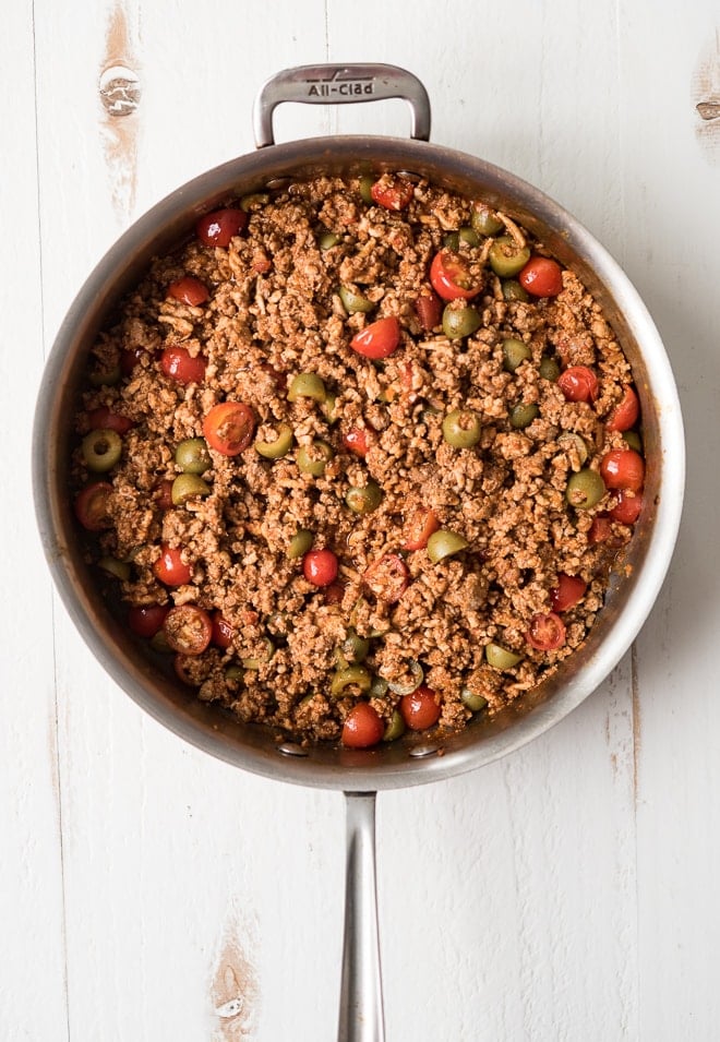 Overhead shot of cooked ground meat in a pan with olives and tomatoes