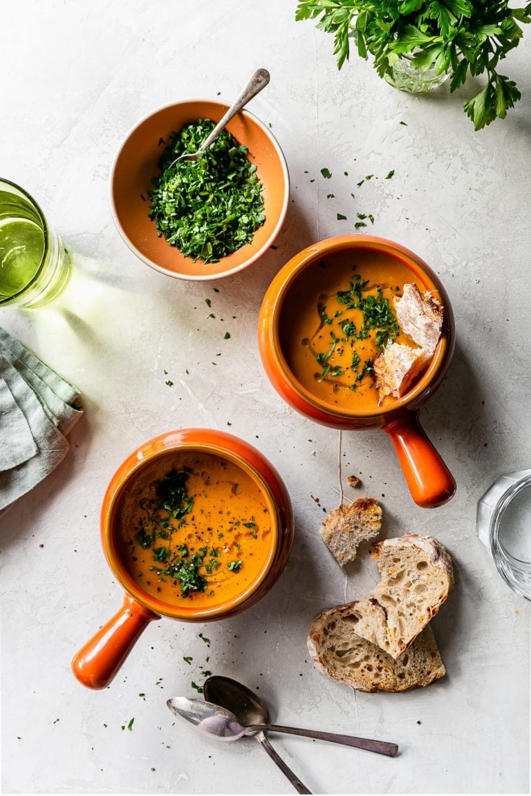 carrot soup in 2 bowls with bread and a bowl of parsley