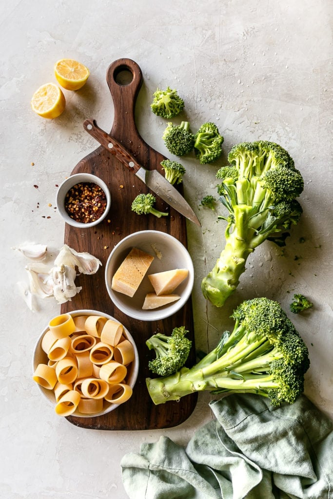 ingredients on a board. broccoli, pasta, parmesan, chili flakes, lemon