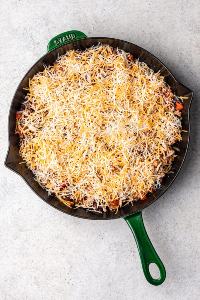 skillet with ground turkey and chopped veggies topped with shredded cheese