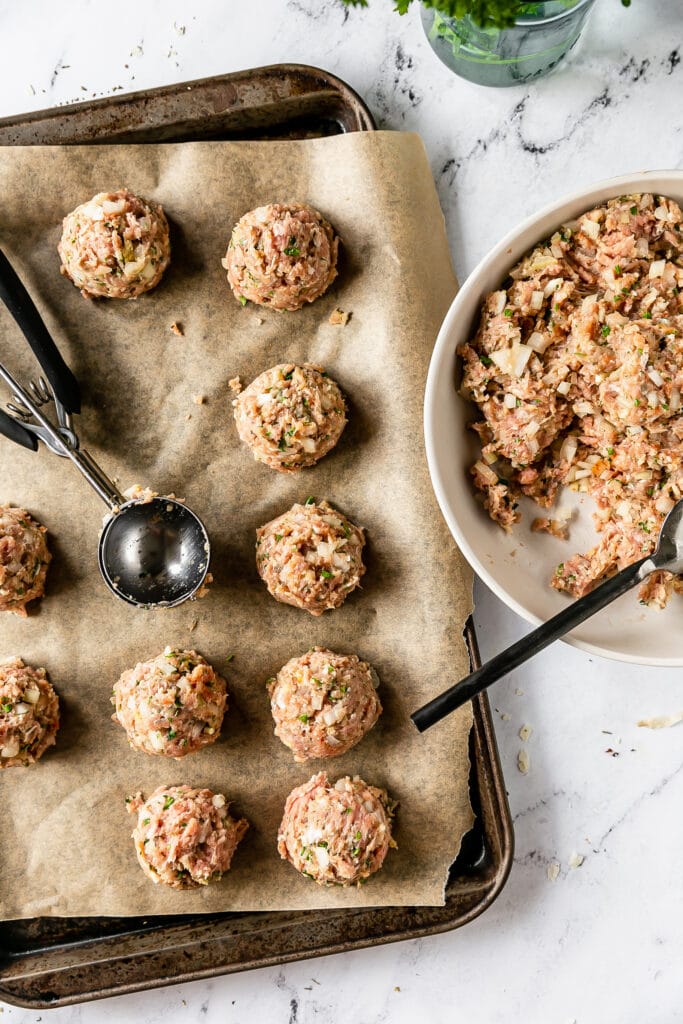 raw meat being formed into meatballs on a cookie sheet using a cookie scoop