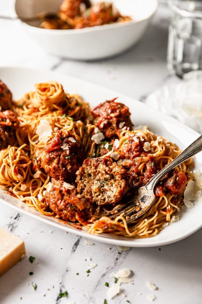 close up shot of a turkey meatballs cut in half with a fork on a serving platter with spaghetti