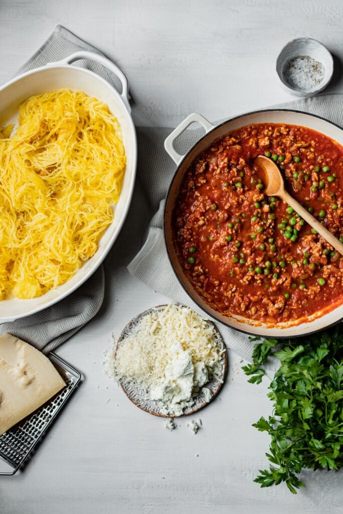 big pot of meat sauce with peas, a baking dish with spaghetti squash and parmesan cheese