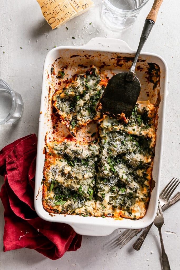 overhead shot of cooked lasagna in a white dish with a spatula
