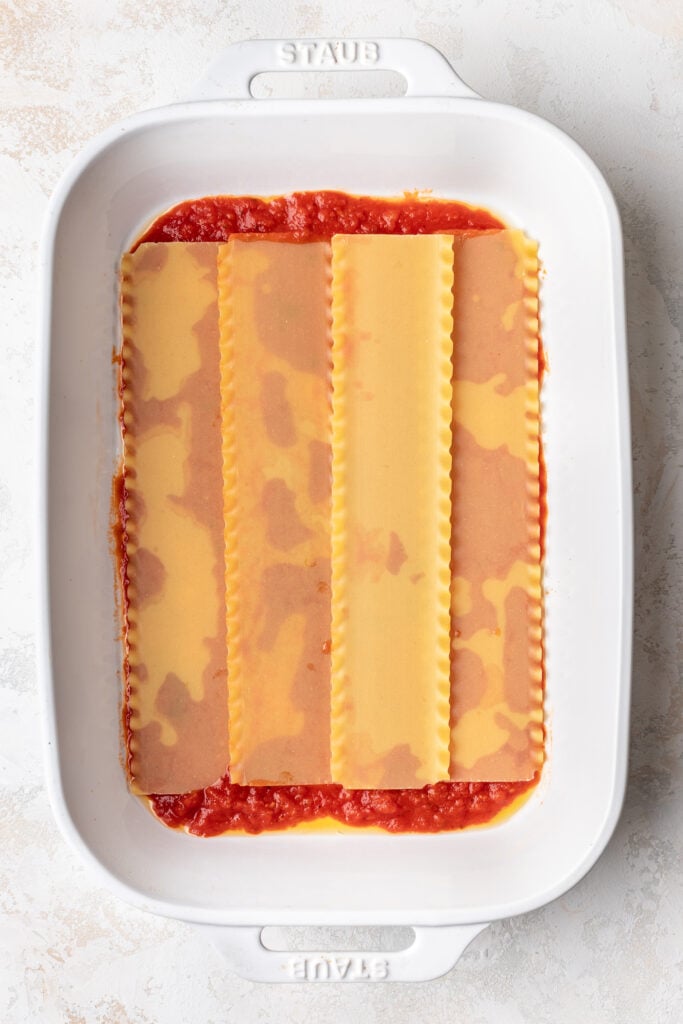 lasagna noodles layered in a baking dish over red sauce