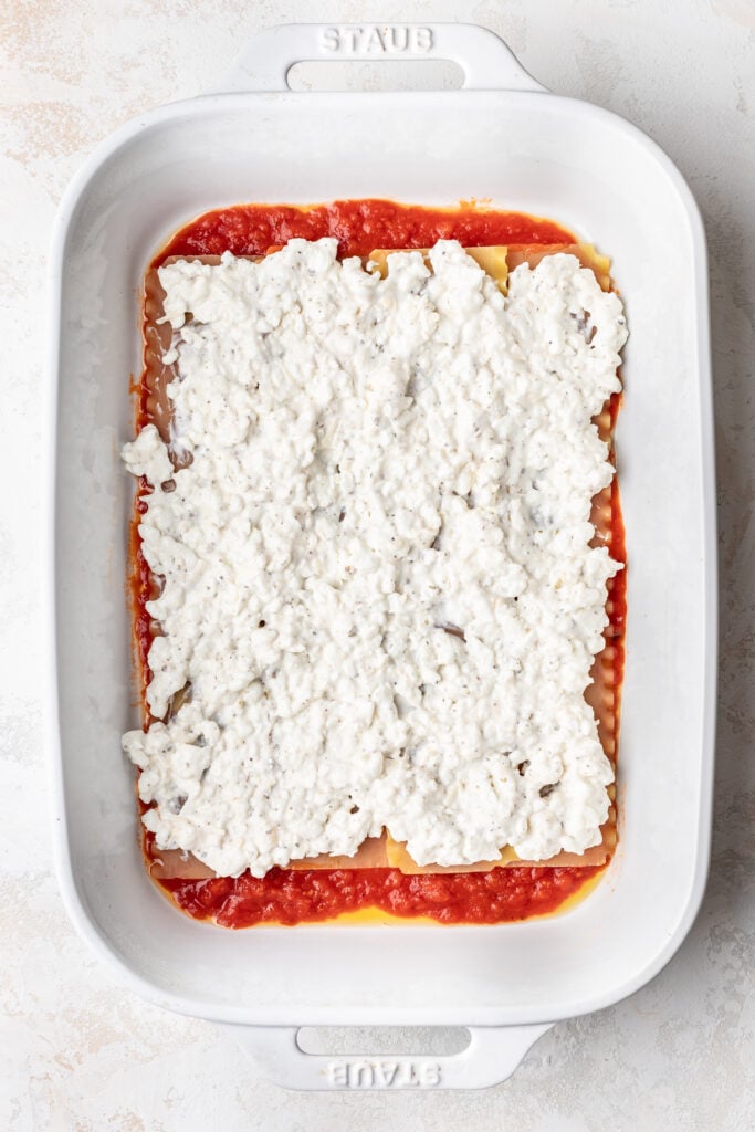 lasagna noodles layered in a baking dish over red sauce with cottage cheese on top