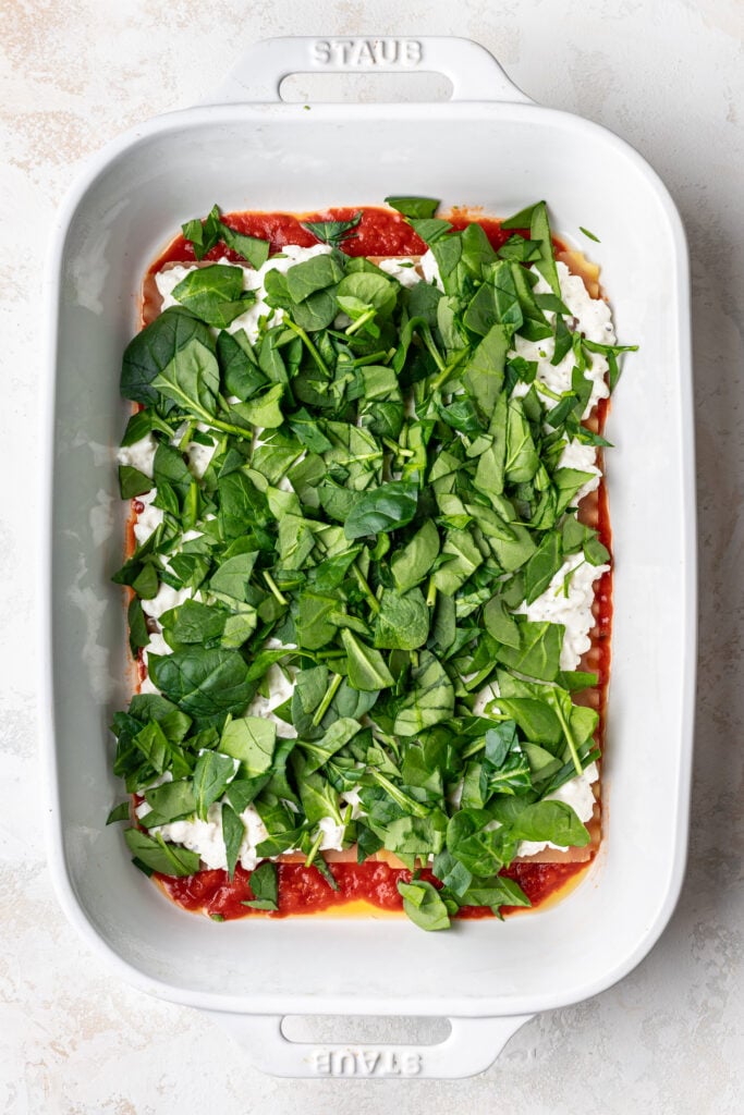 chopped spinach layered in a baking dish for lasagna