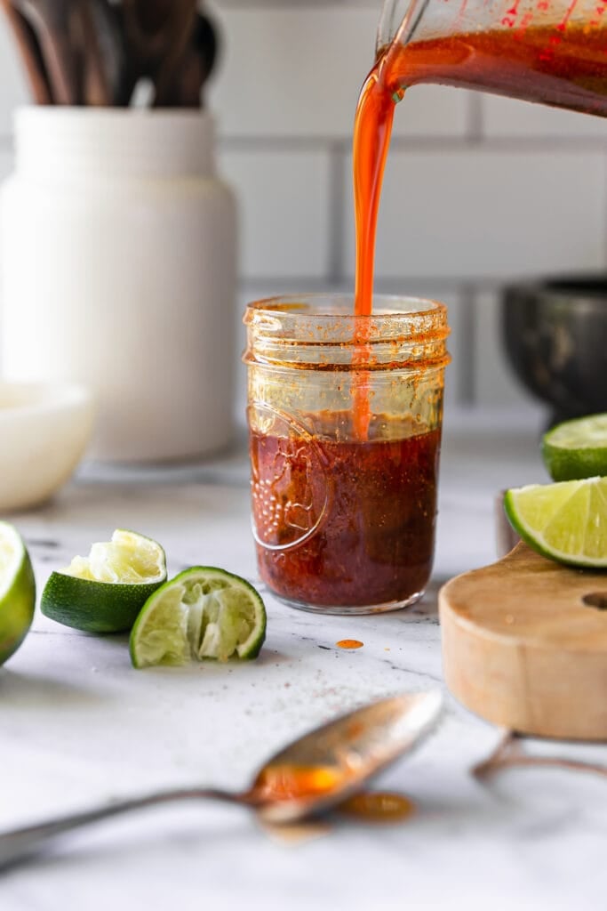 Mexican Lime Chili Marinade being poured into a glass jar with squeezed limes all around