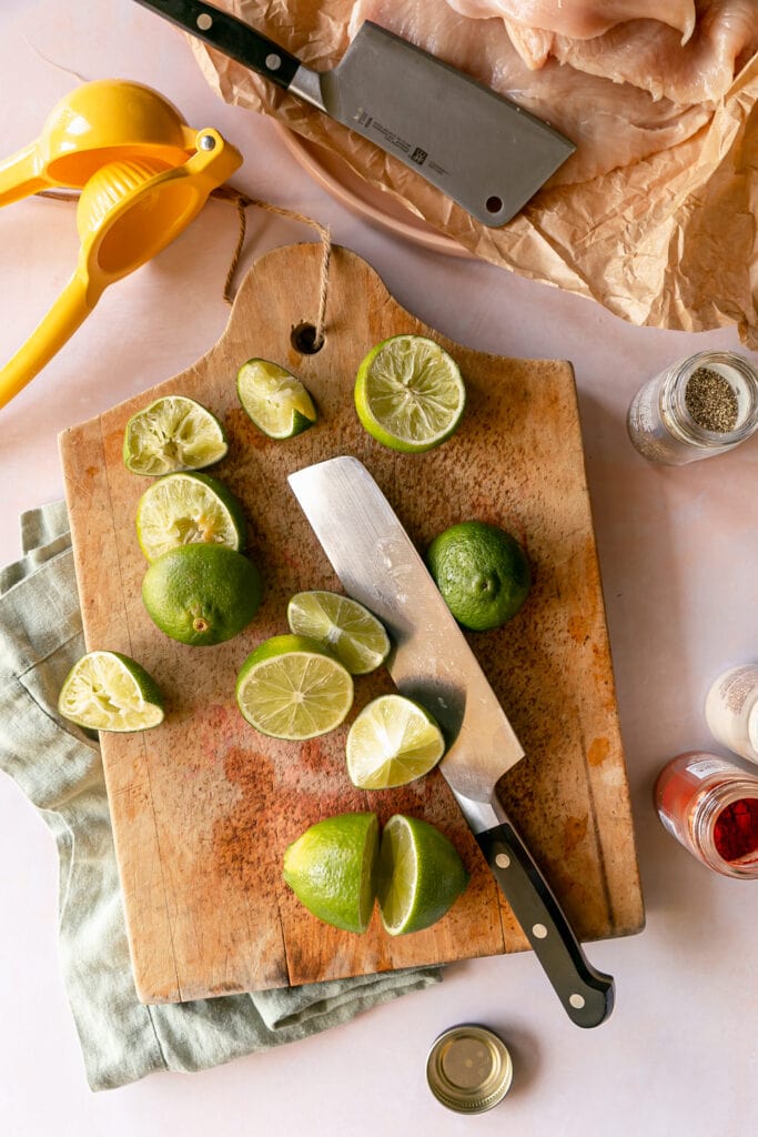 Prep shot of limes being cut on a wood board with large knife