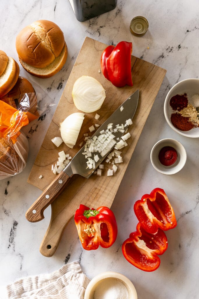 cutting board with diced onion, a large knife and bell pepper