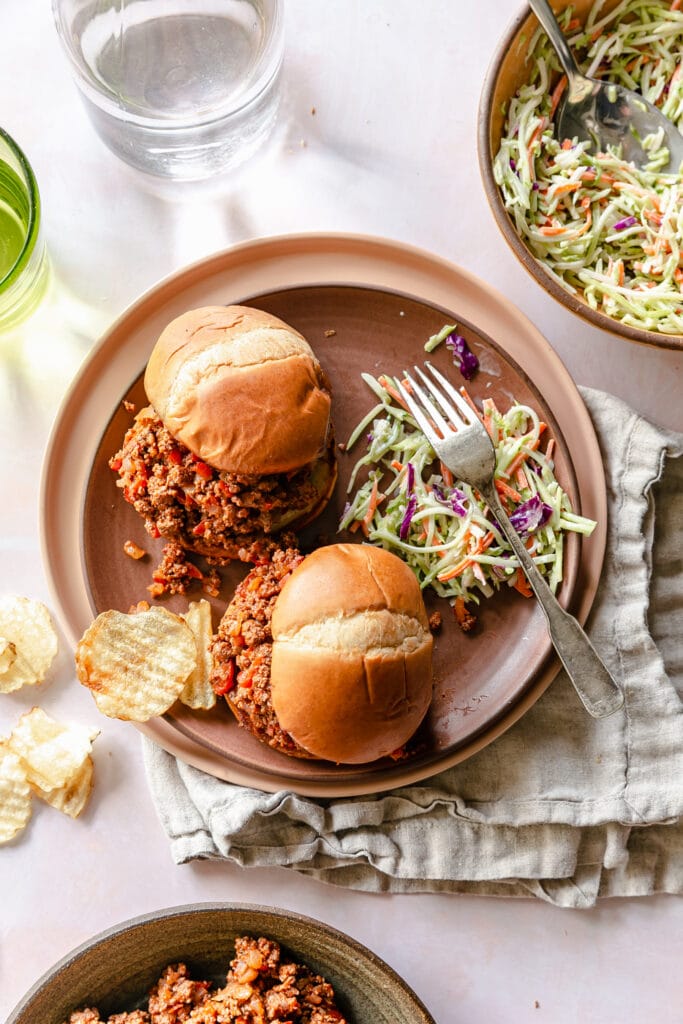 Sloppy Joes on a plate with coleslaw, potato chips and a fork
