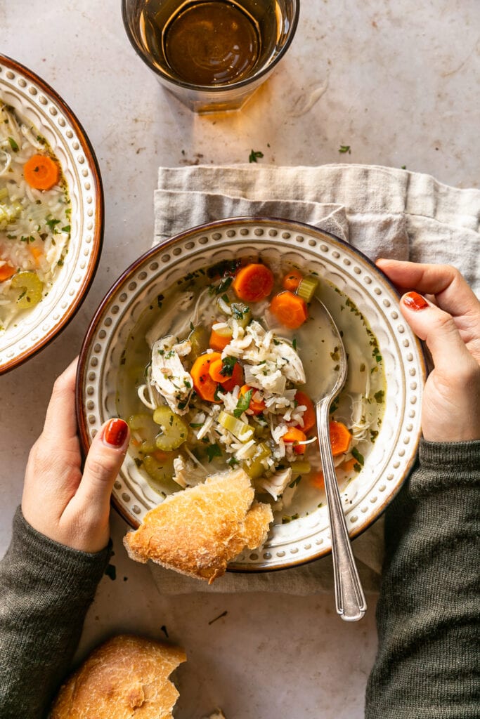Holding soup bowl, cozy sweater, crusty bread and spoon