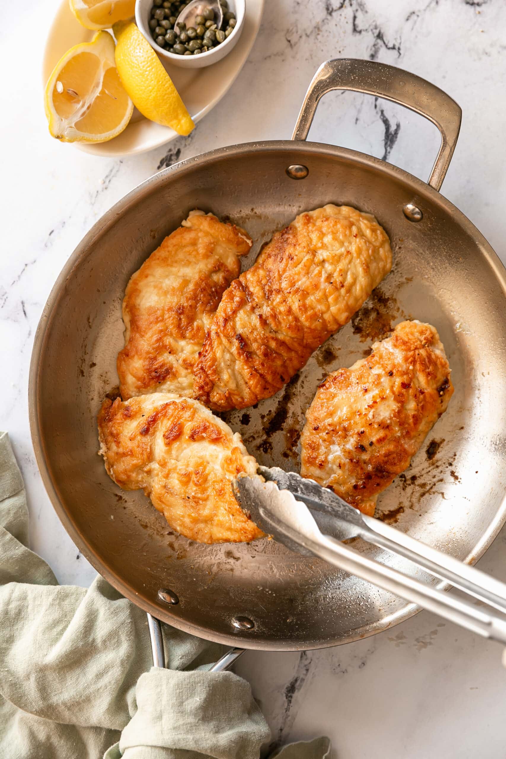 Chicken Piccata in Frying Pan being seared with tongs
