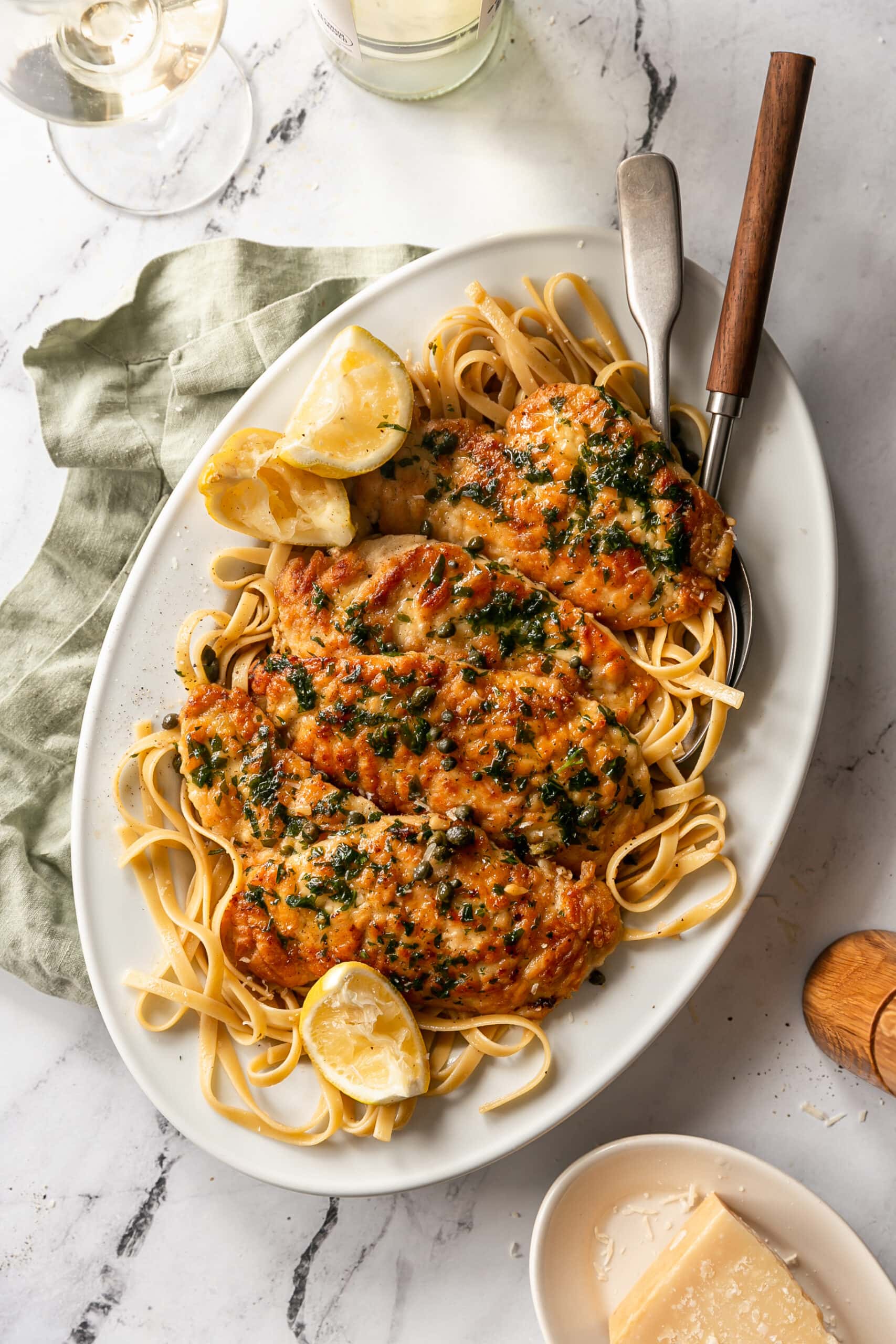 Plated Chicken Piccata with lemon wedges and cooked pasta