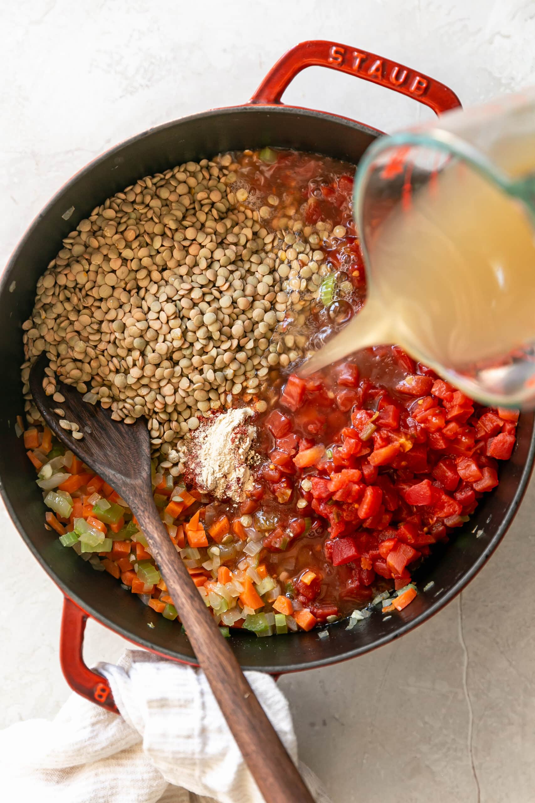 Easy Stovetop Lentil Soup pouring chicken stock into pot with lentils and tomatoes