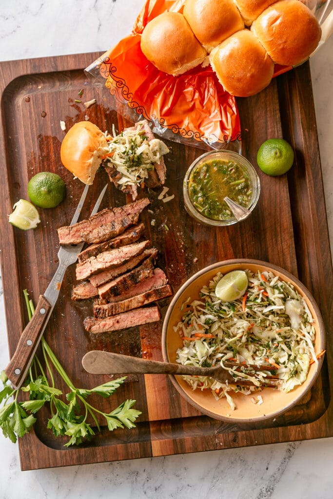 Assembling Steak Sliders on Cutting Board with Chimichurri and Limes
