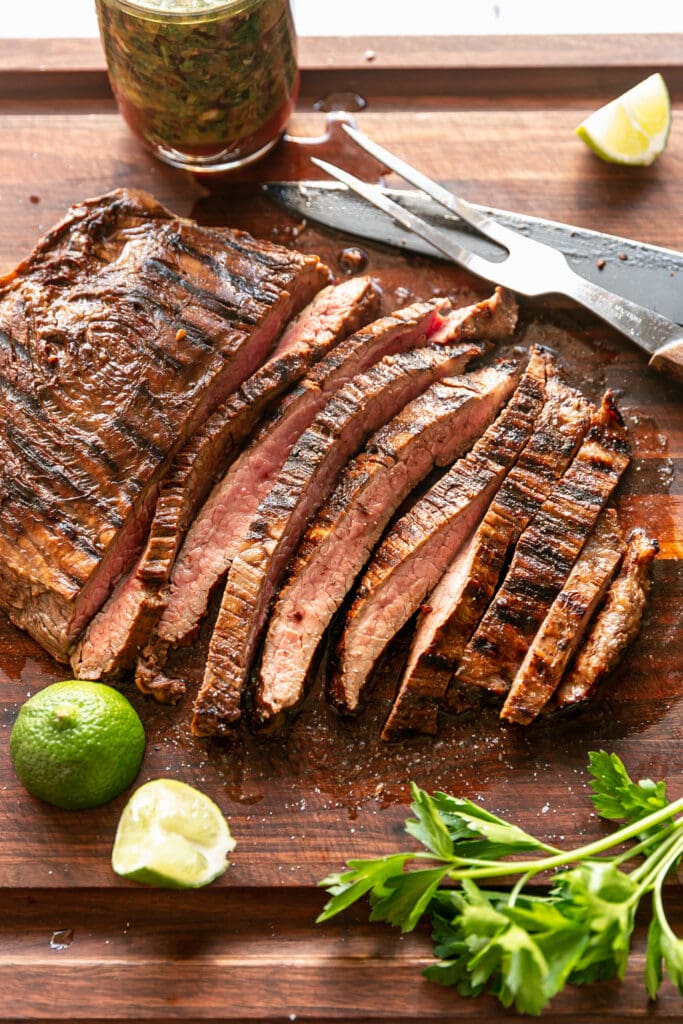 Cooked Flank Steak on Cutting Board with Limes and Parsley