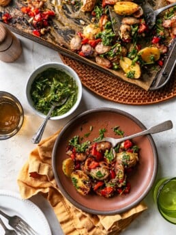 Sheet Pan Sausage and Potatoes cooked sheet pan dinner on table with serving on brown plate chimichurri for serving