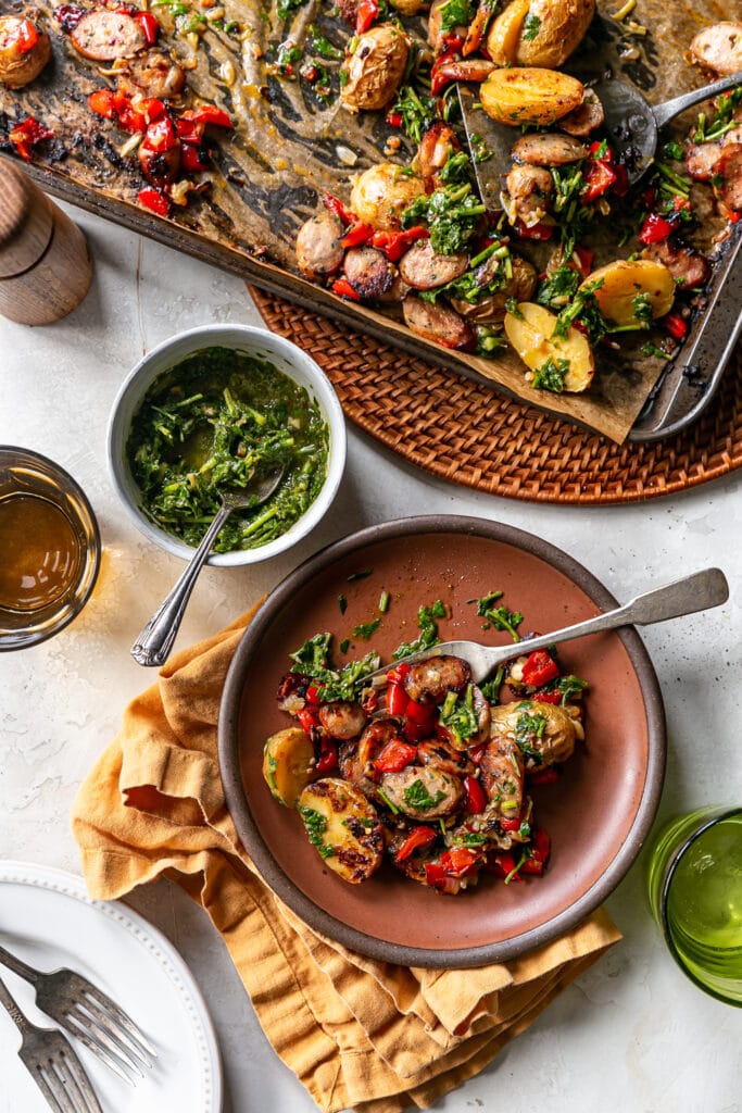 Sheet Pan Sausage and Potatoes cooked sheet pan dinner on table with serving on brown plate chimichurri for serving