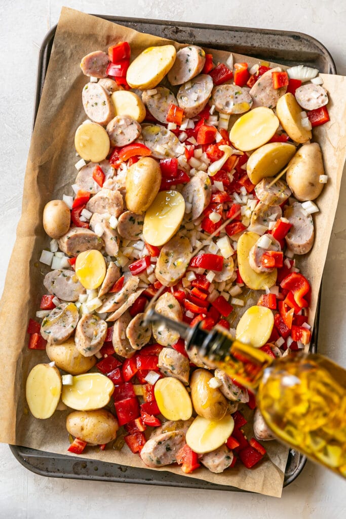 Sheet Pan Sausage and Potatoes onion potatoes red bell pepper and chicken sausage on sheet pan with olive oil drizzled over it