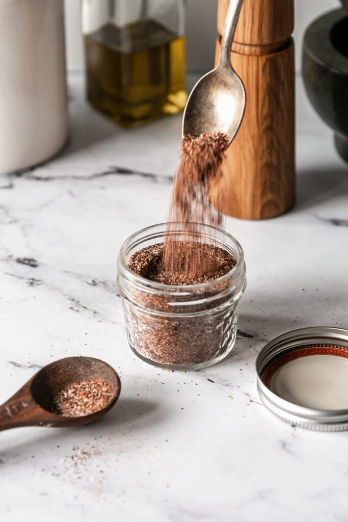 Pouring taco spices from spoon into jar on a marble countertop
