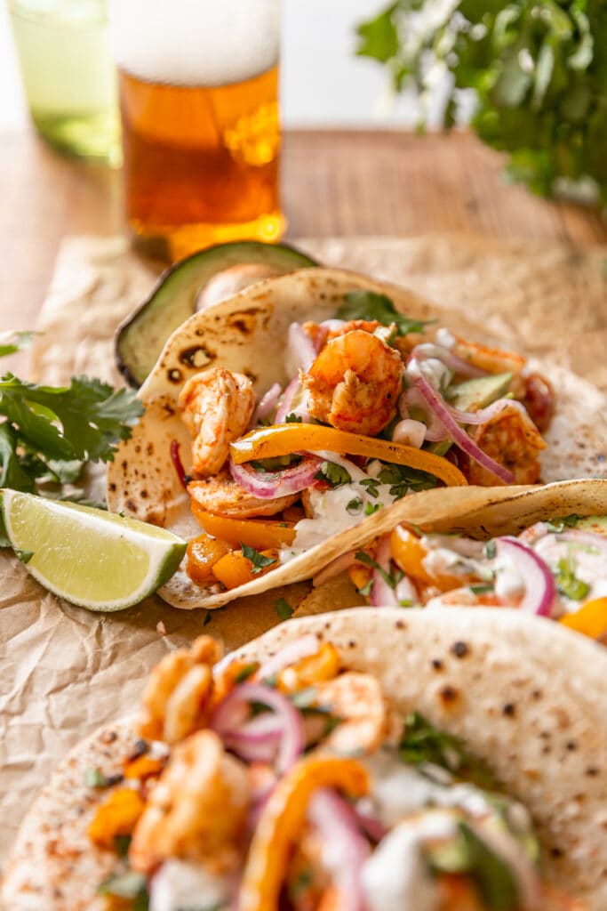 Sheet Pan Shrimp Fajitas with Lime Crema - close up of shrimp tacos on tortillas with limes and beer on parchment paper
