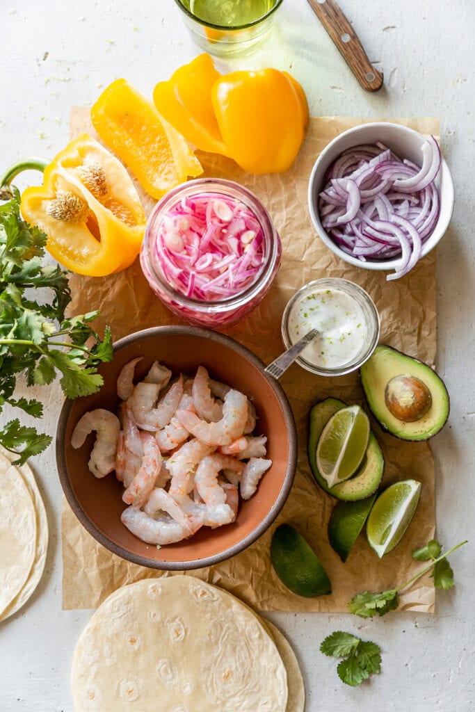 LIBAD Sheet Pan Shrimp Fajitas with Lime Crema - shrimp, bell pepper, onion, avocado, lime, cilantro and tortillas on counter