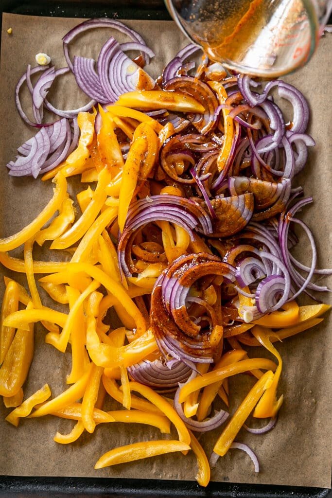 LIBAD Sheet Pan Shrimp Fajitas with Lime Crema - yellow bell pepper and sliced onion on sheet pan with marinade pouring over veggies
