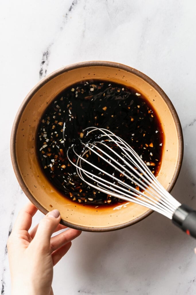 The Best Balsamic Steak Marinade - whisking marinade in orange bowl on marble countertop