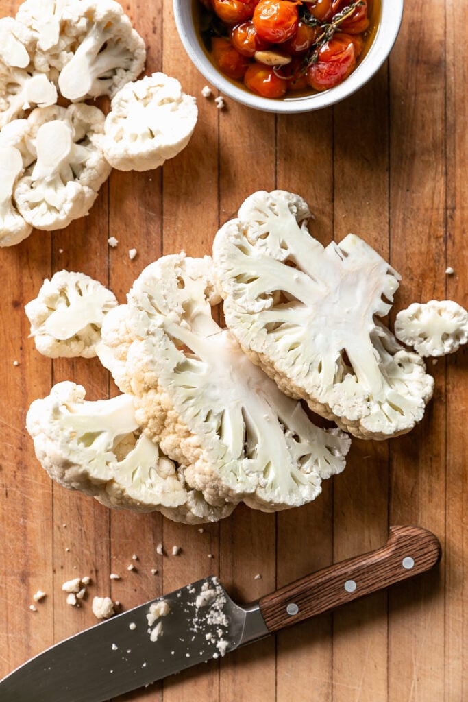 Cauliflower Steaks with Tomato Garlic Confit - cauliflower head sliced into steaks on a cutting board with knife