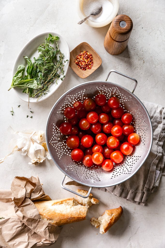 Quick Tomato Garlic Confit - cherry tomatoes in colander with herbs, garlic, red pepper and torn bread