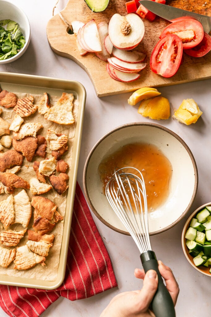 Summer Fattoush Salad - whisking dressing in bowl with toasted torn pita on sheet pan