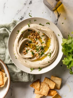 Best 5-Minute Blender Hummus - hummus swirled in bowl with olive oil, pine nuts, pita chips