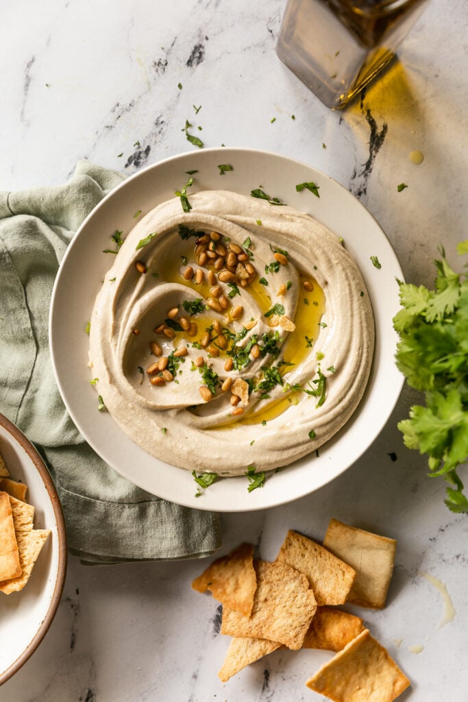 Best 5-Minute Blender Hummus - hummus swirled in bowl with olive oil, pine nuts, pita chips