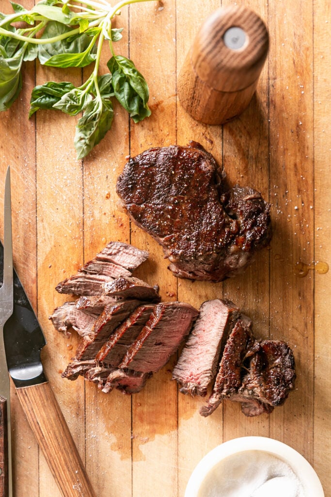 grilled steaks on cutting board sliced with carving knife