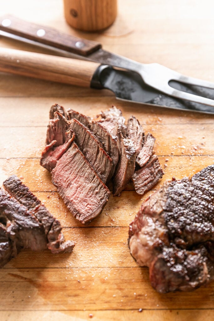 grilled steaks on cutting board sliced with carving knife