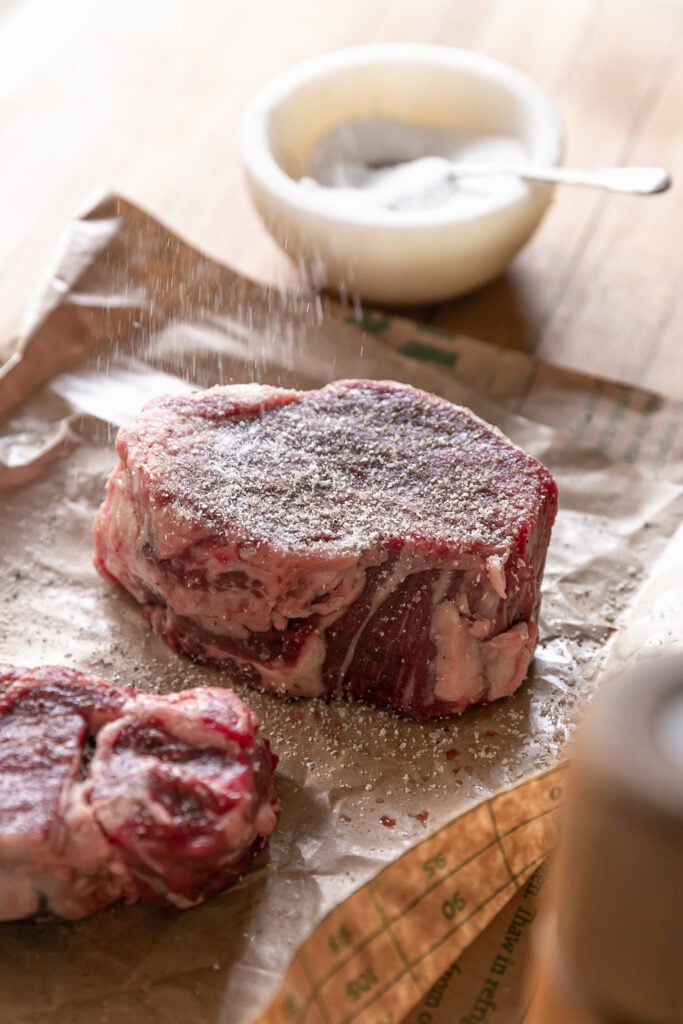 uncooked steak sprinkled with salt in brown paper