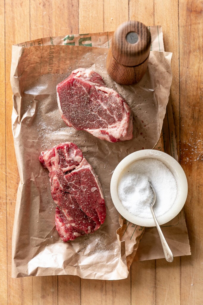 uncooked steaks seasoned with salt and pepper in brown paper