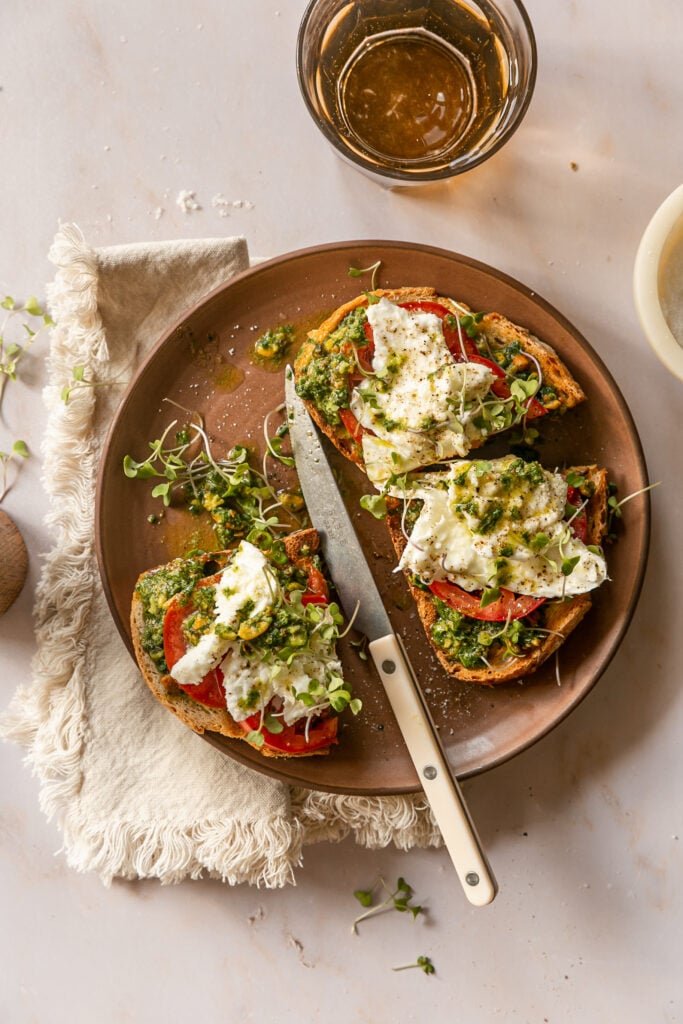 pesto on toast with tomato, burrata and microgreens on plate with knife