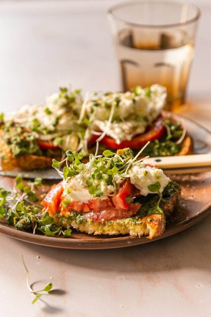 pesto on toast with tomato, burrata and microgreens on plate with knife