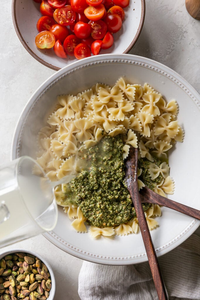 pouring hot pasta water into bowl with pasta and pesto in a bowl