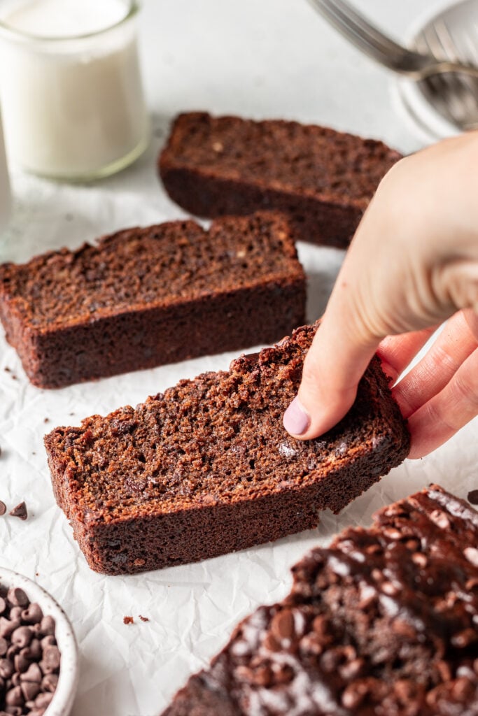 a hand breaking a piece of chocolate banana bread
