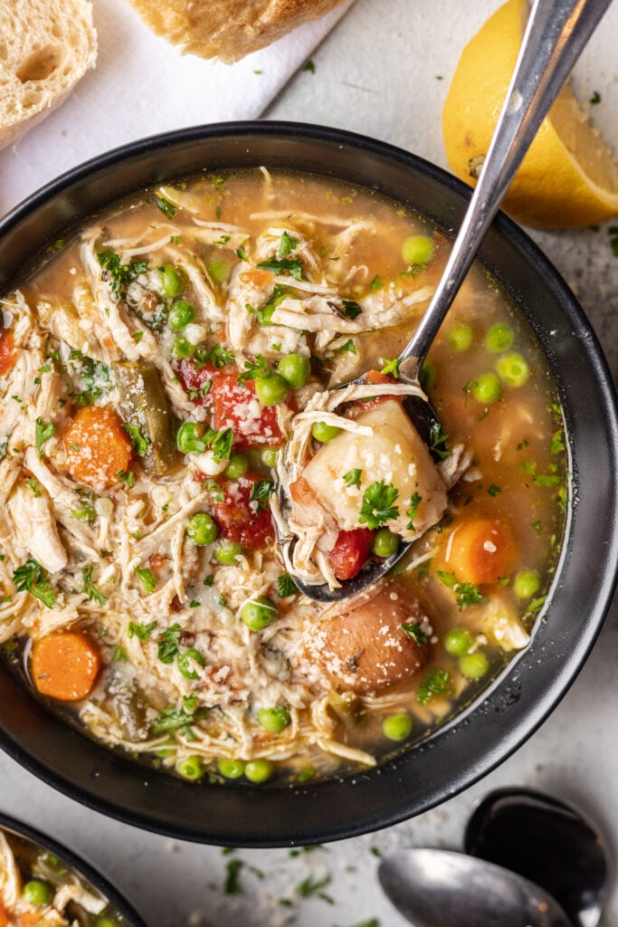 black bowl full of chicken vegetable soup with a spoon in it
