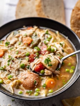 black bowl full of chicken vegetable soup with a spoon in it