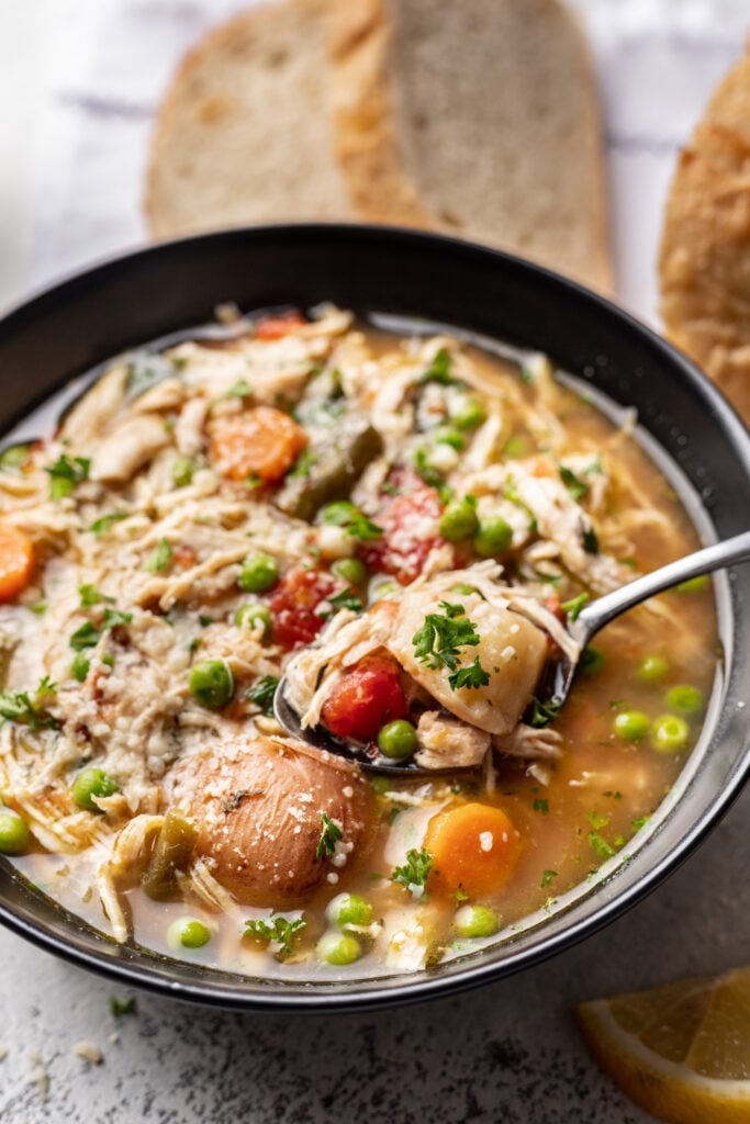 chicken veggie soup in a black bowl with a spoon and bread on the side