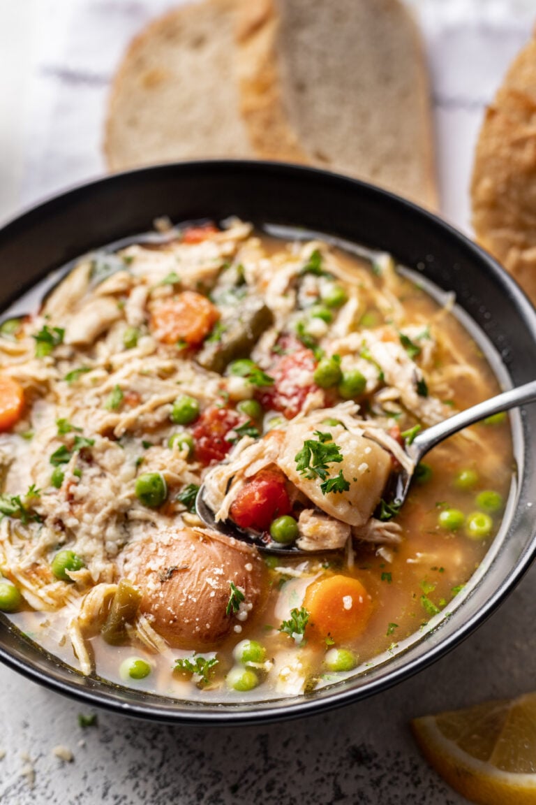 black bowl full of chicken vegetable soup with a spoon in it