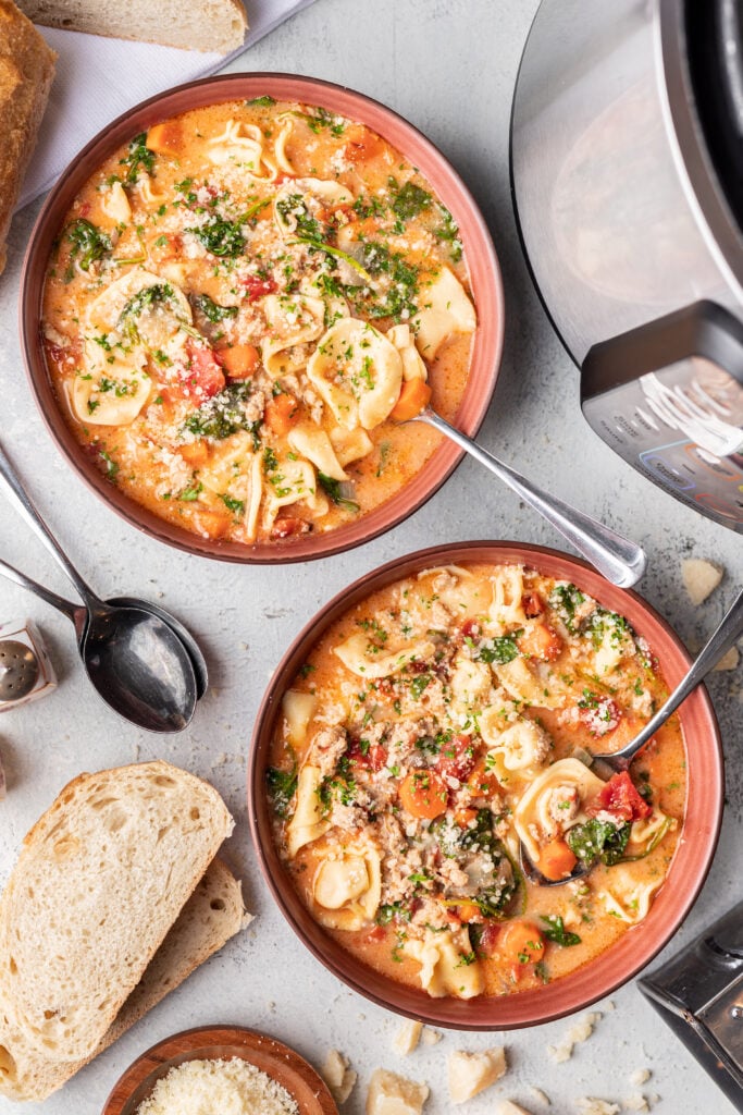 tortellini soup in two bowls with parmesan cheese and spoons