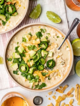 white chicken chili in a bowl with jalepenos, cheese and avocado on top with a spoon
